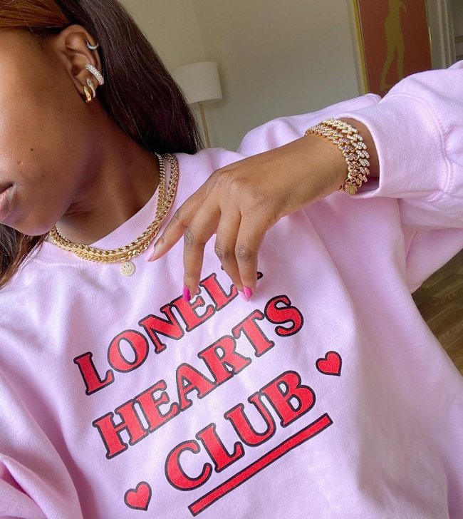 acessorios-dourados-colar-correntes-nnennaechem Garota usando colares e pulseiras de correntes e um moletom rosa escrito Lonely Hearts Club em vermelho