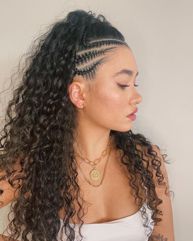 cabelo-cacheado-com-tranca-lateral Foto de uma mulher de perfil. Ela usa um top cropped branco, colares dourados, cabelo cacheado solto com trança lateral na raiz do cabelo. Ela está de perfil, não olha para a câmera e não sorri.