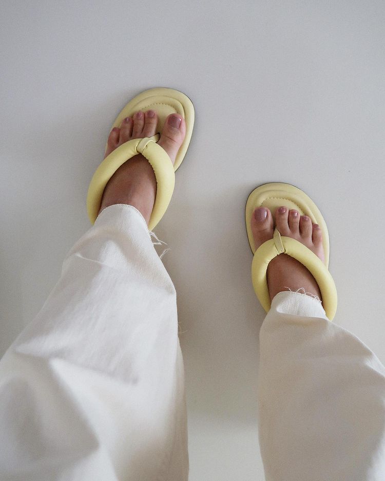 chinelo-tendencia-verao-2022 Pés usando chinelo amarelo e parte da perna com calça branca
