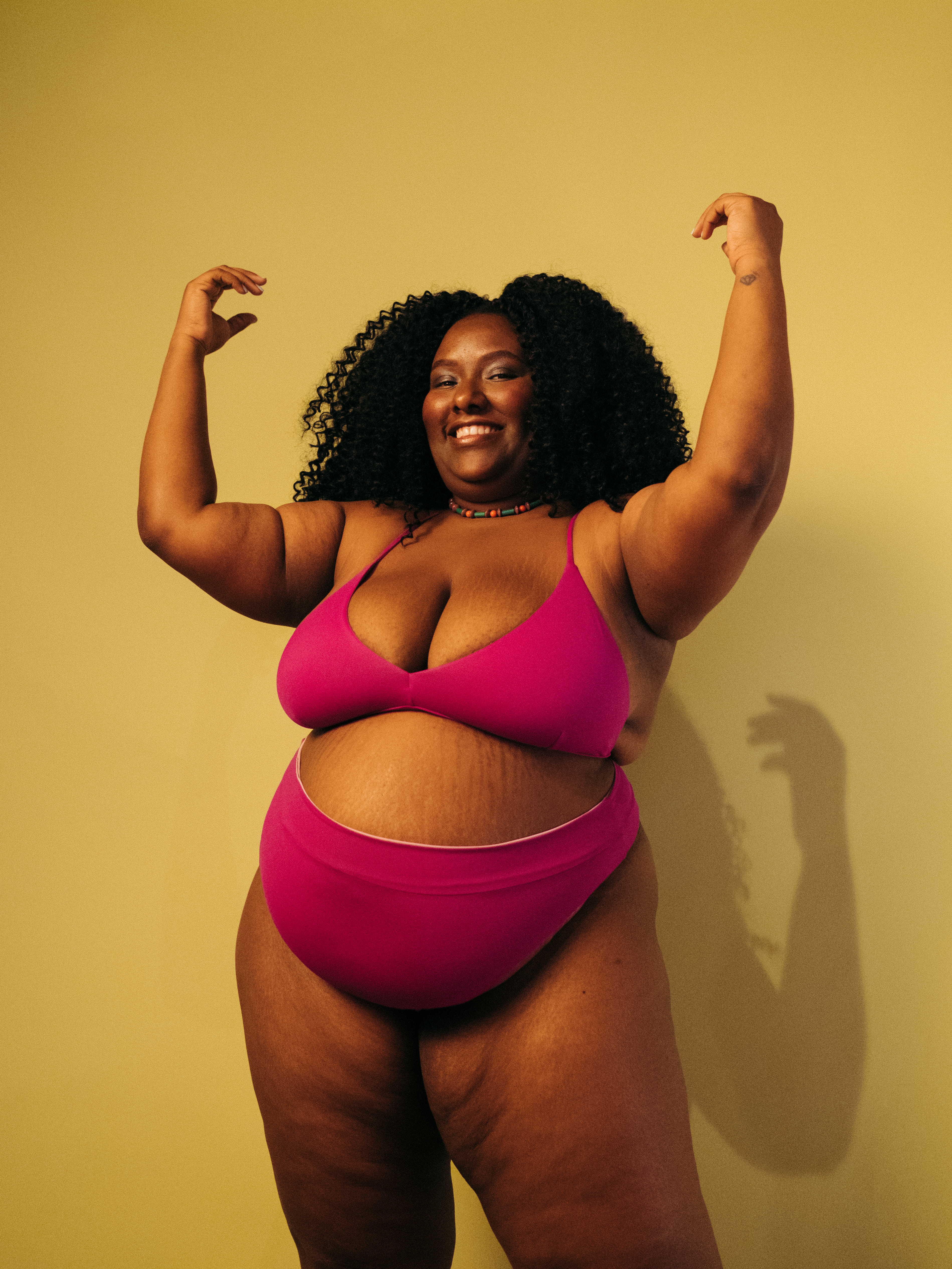 colecao-biquinis-lela-brandao-co Modelo usando biquíni rosa, sorrindo e com os braços levantados