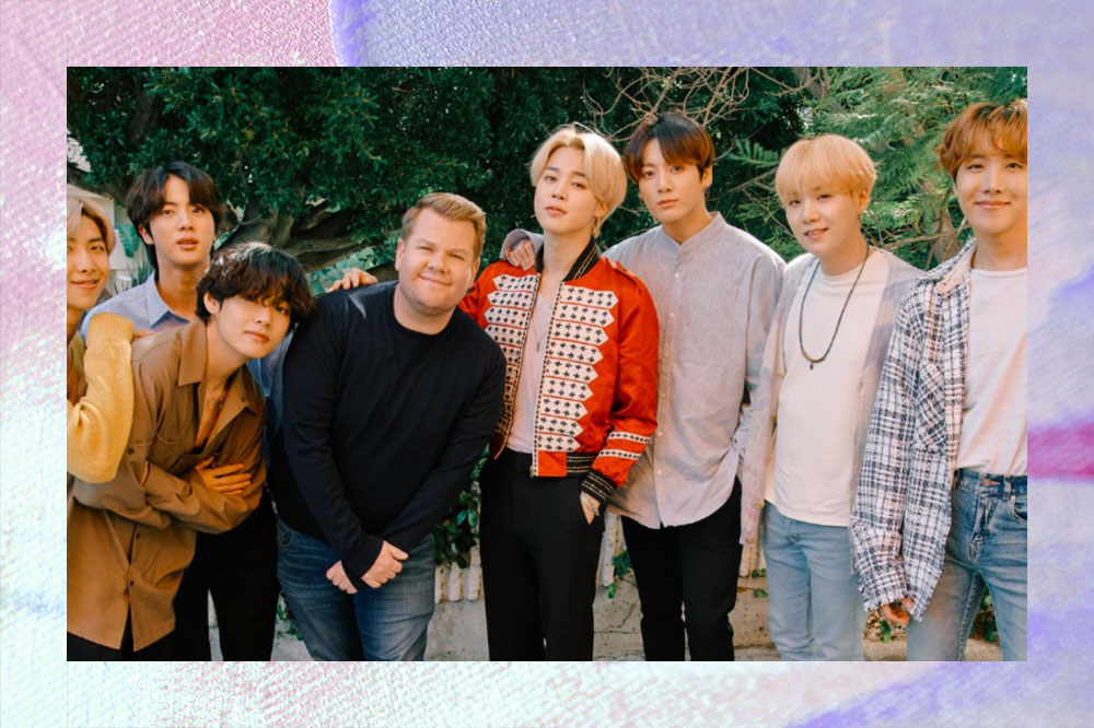 Foto de James Corden posando ao lado dos integrantes do BTS ao ar livre.