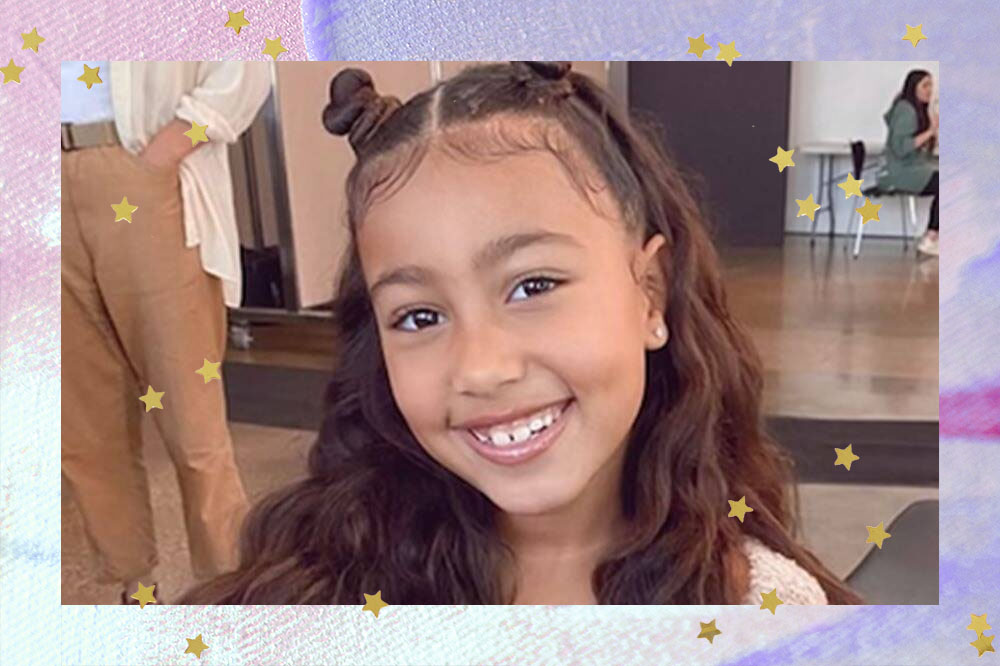 Foto de North West. Nela, a menina aparece sorrindo com cabelo arrumado em penteado.