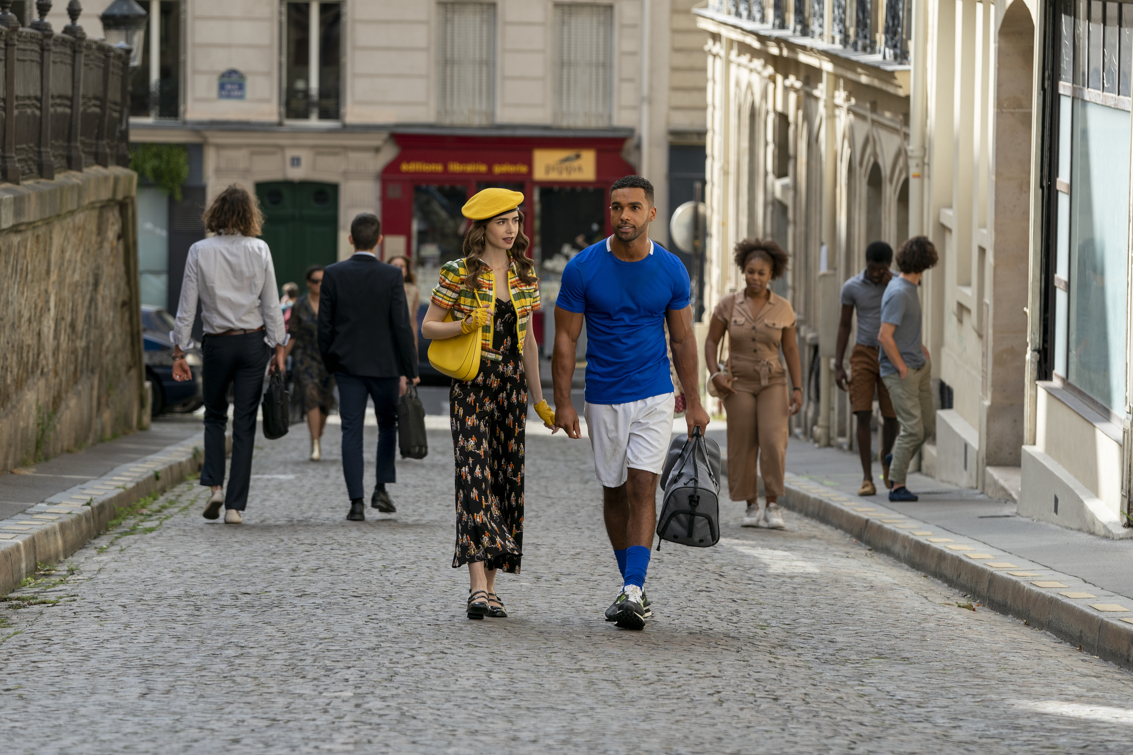 figurino-emily-em-paris-segunda-temporada-05 Lily Collins como Emily e Lucien Laviscount como Alfie de mãos dadas na série Emily em Paris