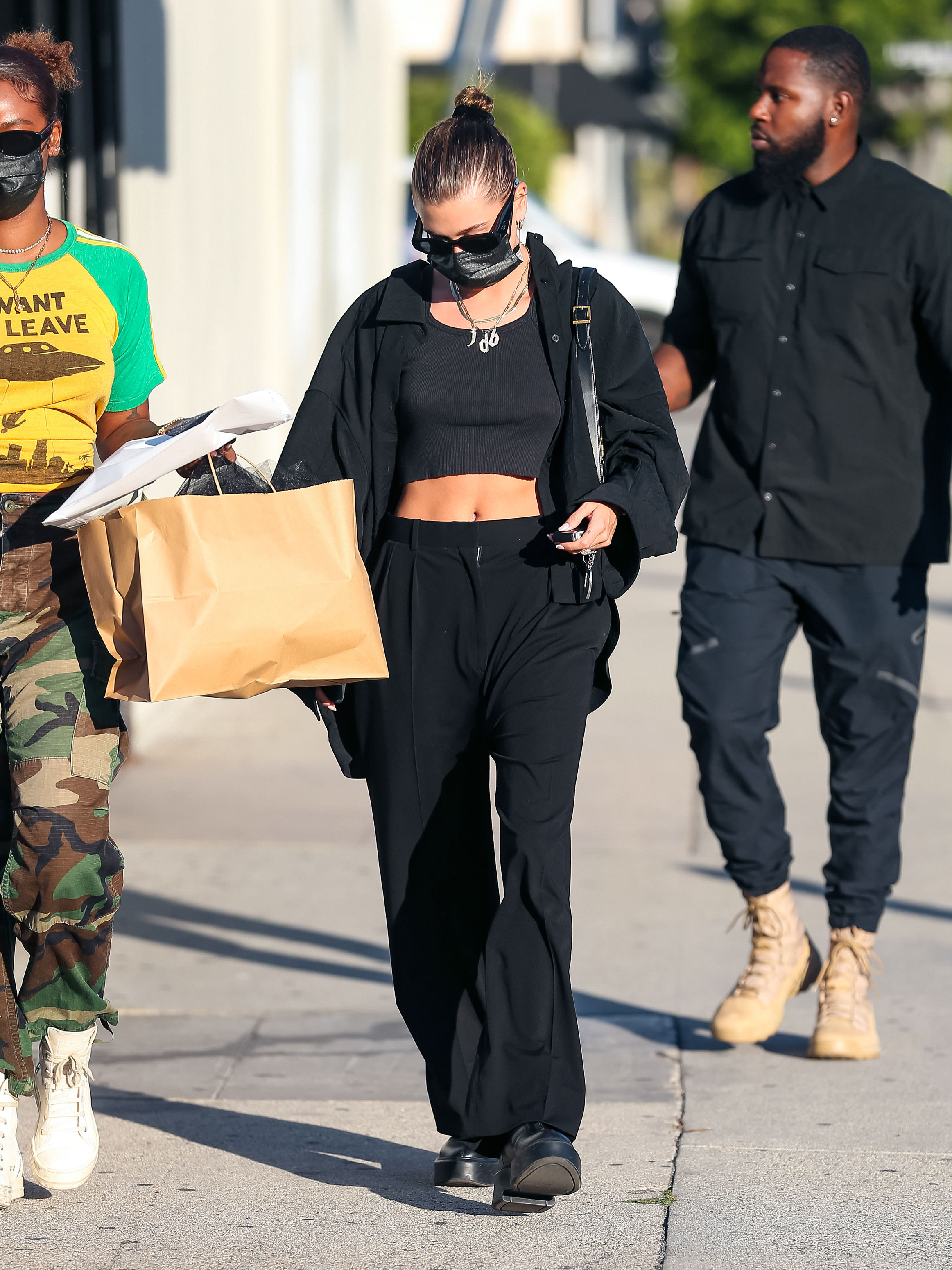 Celebrity Sightings In Los Angeles – October 29, 2021 Hailey Bieber usando look todo preto com top cropped, calça de alfaiataria, camisa, tênis, bolsa pendurada no ombro, máscara de proteção facial e óculos escuros