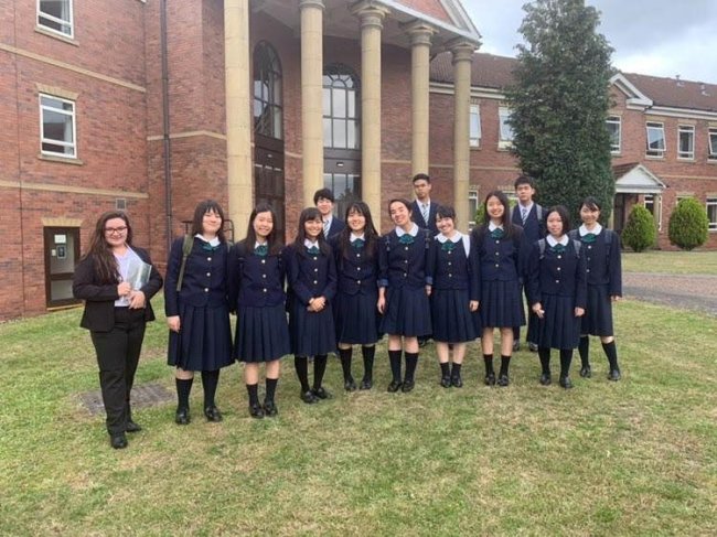 Como é morar em um internato no interior da Inglaterra? Foto de Marine, da Galera CH, em seu primeiro dia de aula no intercâmbio. Ela está de calça e terninho preto, e posa ao lado dos colegas de sala