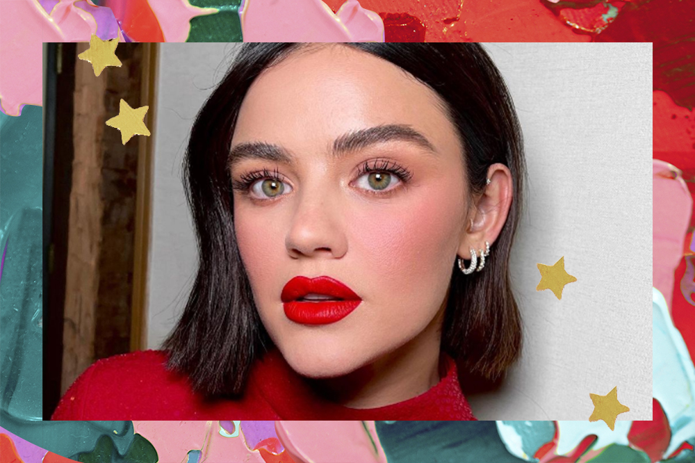 Lucy Hale com expressão facial séria usando batom vermelho. O fundo da montagem tem tintas em rosa, vermelho e verde e estrelinhas douradas.