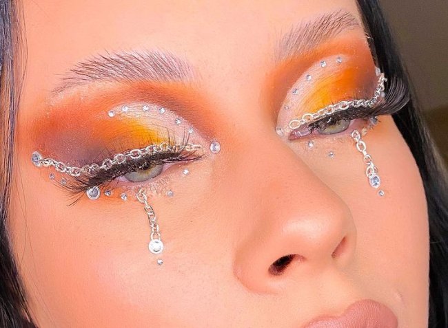 maquiagem-com-correntes Foto dos olhos de uma mulher. Os olhos estão com uma sombra laranja e com detalhe de correntes.