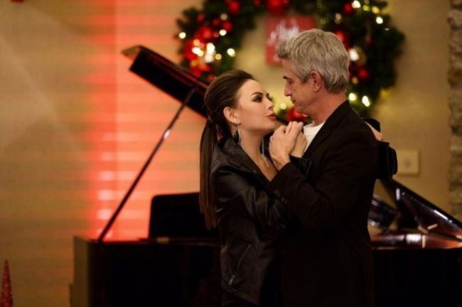 o-natal-foi-cancelado Uma mulher e um homem dançando juntos em frente a um piano, com roupas pretas.