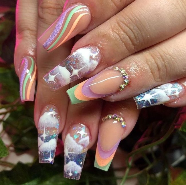 unha-colorida-com-nuvens Foto de duas mãos com as unhas coloridas com decoração de nuvens brancas.