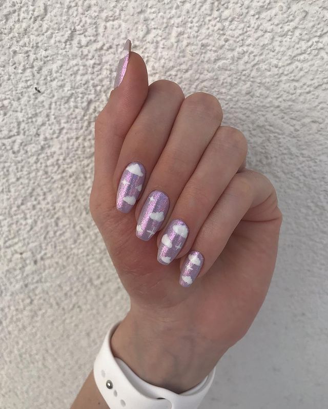 Foto de uma mão com unhas holográficas com decoração de nuvens brancas.