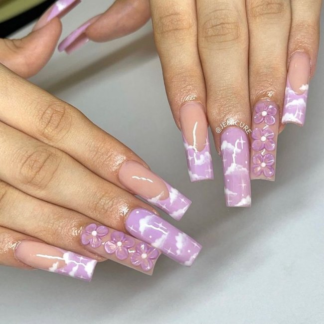 Unhas com esmalte lilás e decoração de nuvens brancas.