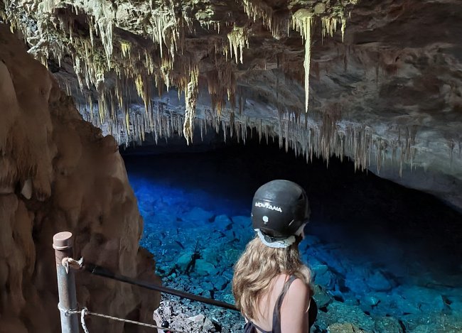 foto azul – gruta Foto da integrante da Galera, Antonela Andrade, em uma gruta com águas cristalinas, em Bonito. Antonela é branca dos cabelos loiros.