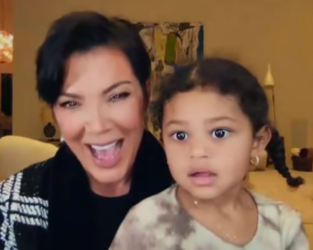 Captura de tela de entrevista em que Kris Jenner está rindo enquanto segura Stormi sentada em seu colo com expressão confusa e sorrindo levemente