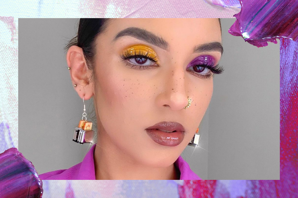 Garota usando maquiagem com um olho de cada cor, um com sombra amarela e o outro com sombra roxa. Sua expressão facial é séria e o fundo da montagem é roxo, rosa e lilás.