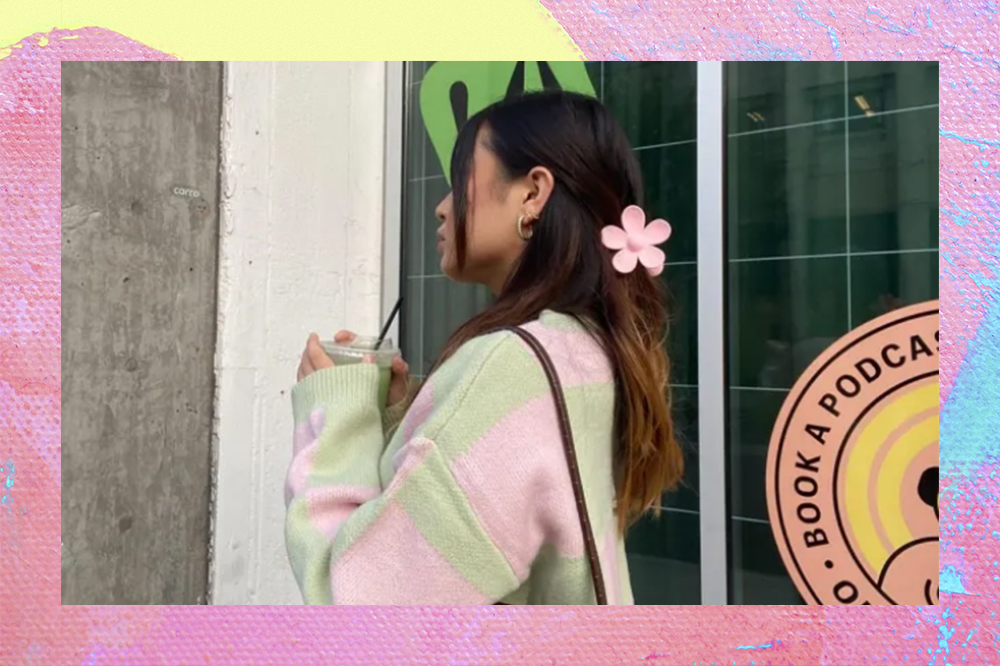 Garota de lado usando cardigan verde e rosa com presilha em formato de flor rosa presa no cabelo. O fundo da montagem é rosa, amarelo e azul