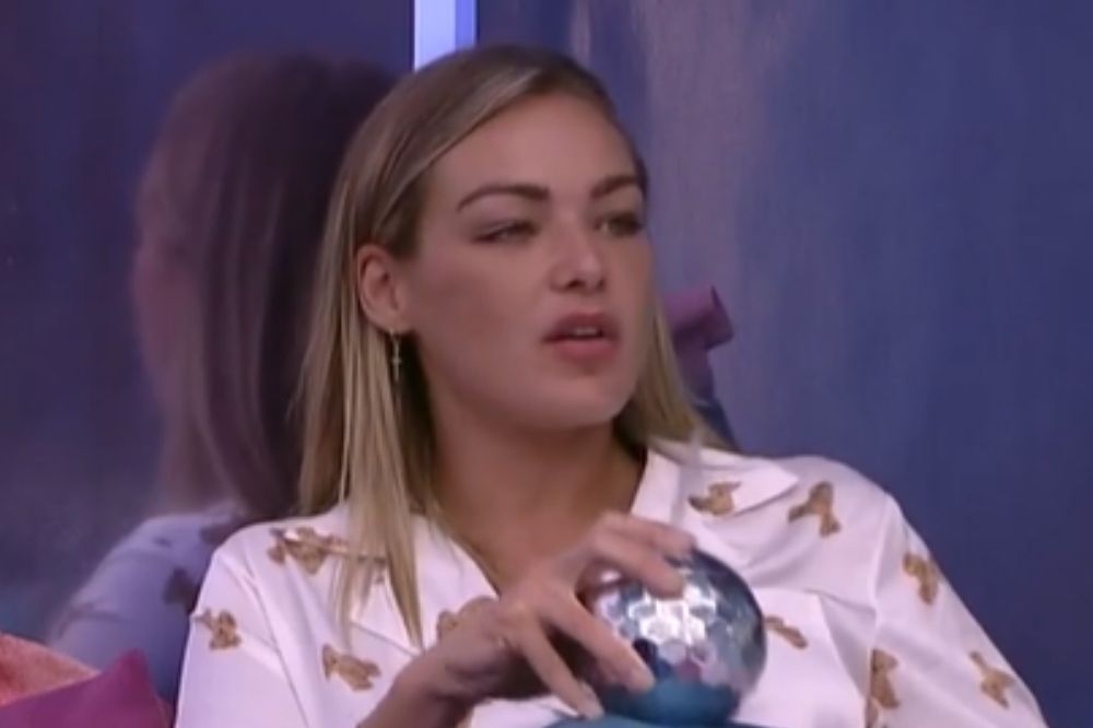 Bárbara, do BBB22, no quarto do líder deitada na cama enquanto fale e segura um mini globo de festa espelhado