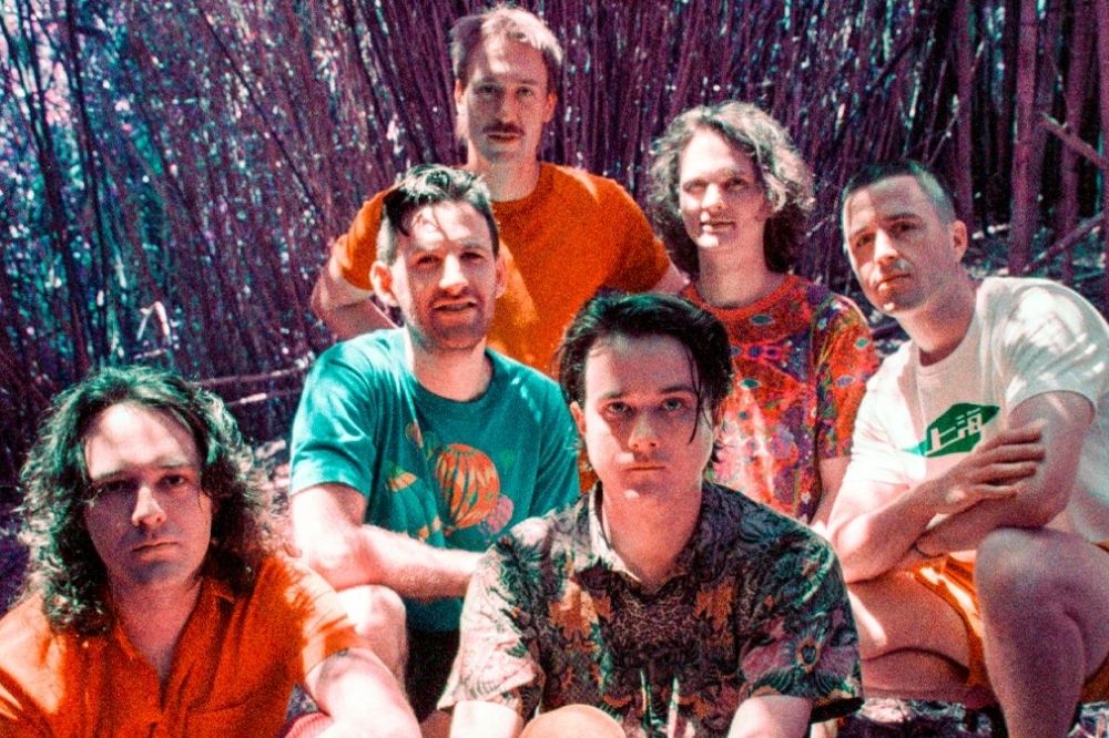 Imagem da banda King Gizzard & The Lizard Wizard posando para foto com o sol refletindo no rosto dos seis integrantes que usam roupas coloridas em tons de laranja, verde, azul e preto