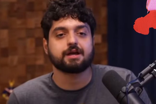 Print de Monark falando no microfone do podcast Flow. Ele tem barba e cabelo pretos