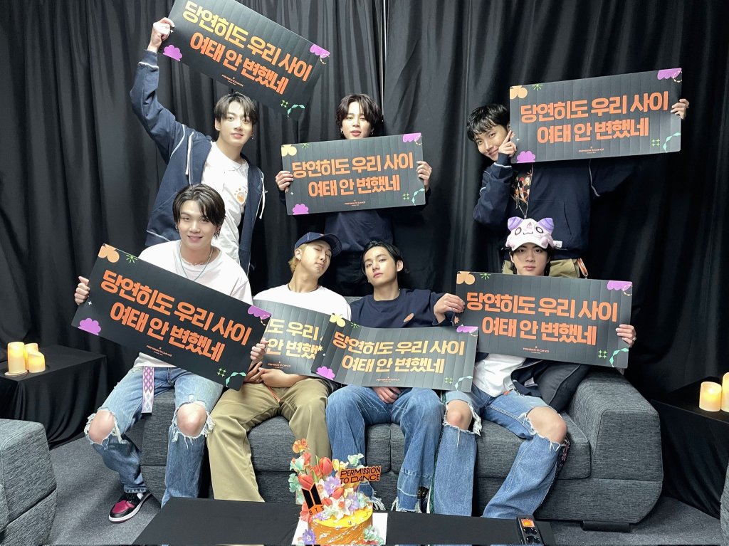 BTS sentados num sofá segurando placas.