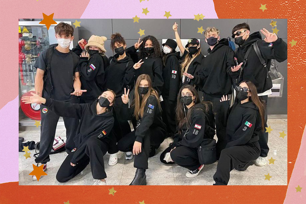 Imagem mostra integrantes do Now United reunidos em sua chegada ao Brasil. O grupo veste um uniforme de moletom preto com numeração e as respectivas bandeiras dos países. A montagem segue acompanhada de uma borda colorida e estrelinhas douradas por toda a imagem.  