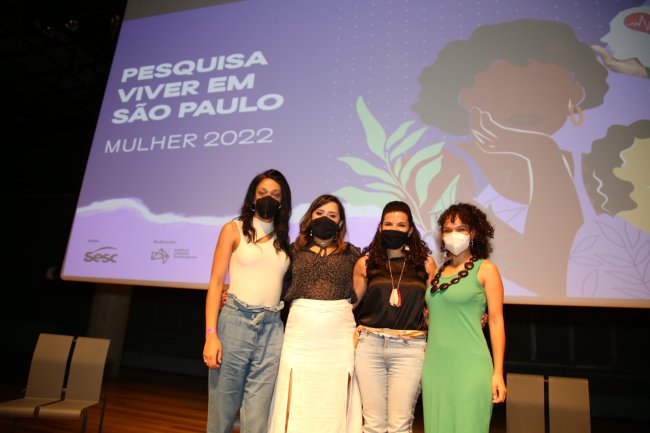 1 em cada 3 jovens paulistanos presenciou violência doméstica em 2021 Quatro mulheres posam no palco, em frente à foto de divulgação de uma pesquisa sobre ser mulher em São Paulo. Estão todas de máscara.
