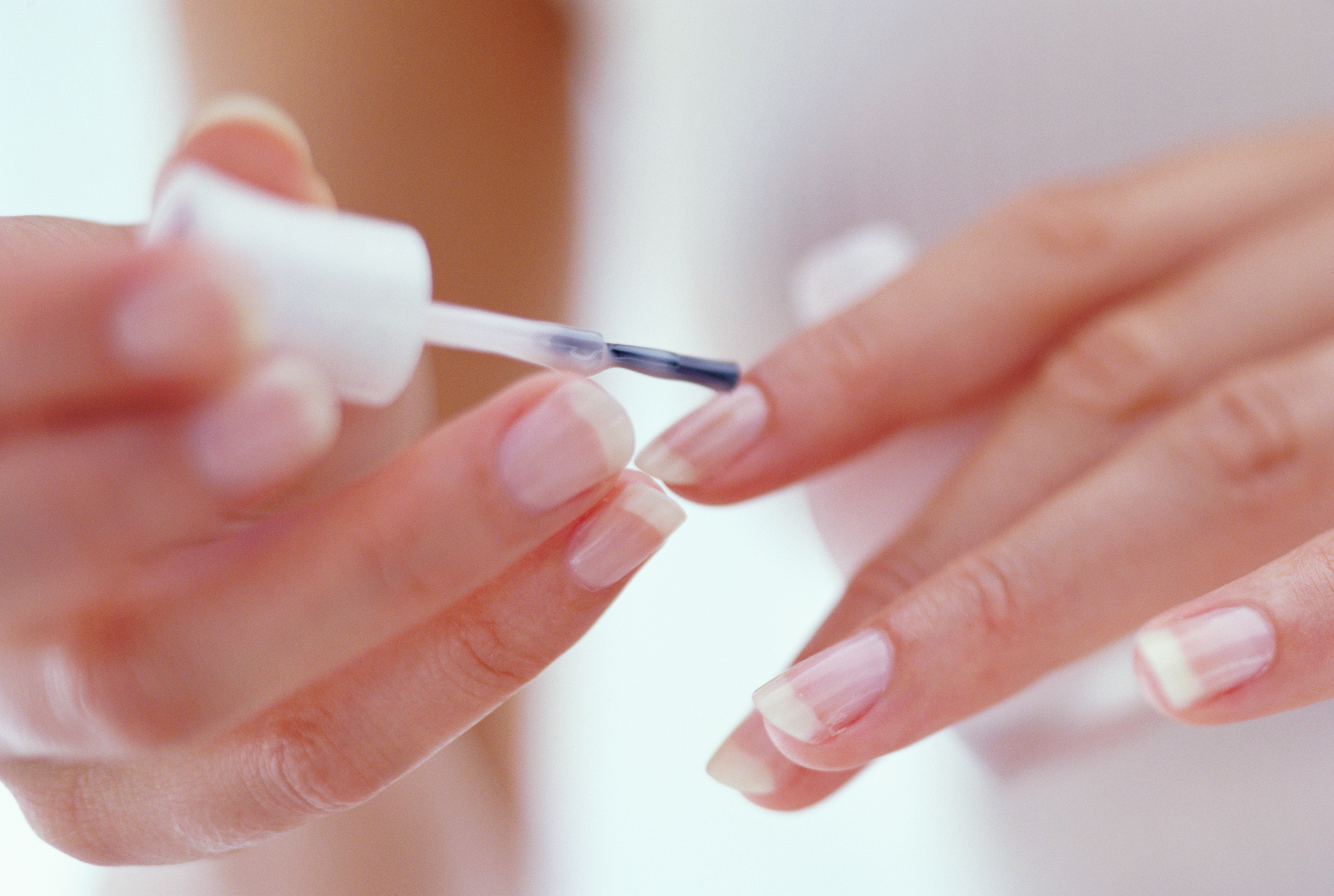 Mulher jovem pintando as unhas com base transparente. A imagem destaca esse processo em close-up, plano da câmera que possibilita uma visão próxima e detalhada da fotográfica.