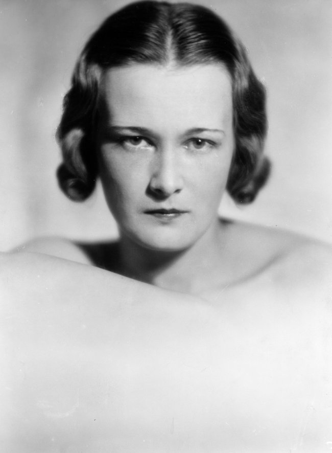tendencia-sobrancelhas-anos-30 Foto em preto e branco de 1933 de uma campanha da Coco Chanel com a foto de uma mulher com o cabelo curto, maquiagem simples e sobrancelha marcada e fina. A modelo olha para a câmera e não sorri