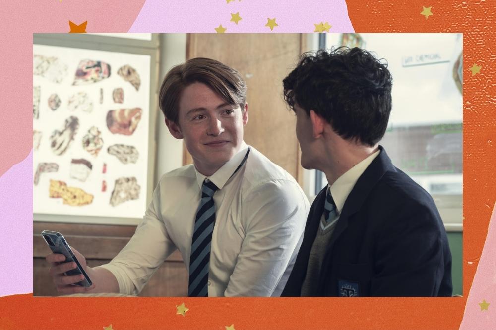 Montagem com o fundo colorido em tons de rosa e laranja com detalhes de estrelas douradas com a foto de uma cena de Heartstopper no centro. A imagem mostra Nick e Charlie ne escola usando uniformes escolares sentados um ao lado do outro conversando.