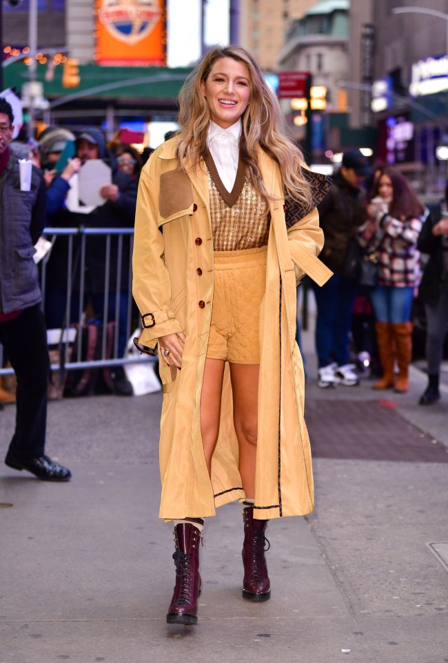 look-bege-e-marrom-blake-lively Foto Blake Lively com blusa marrom e bege, bermuda bege e casaco alongado bege. Ela está na rua e sorri.