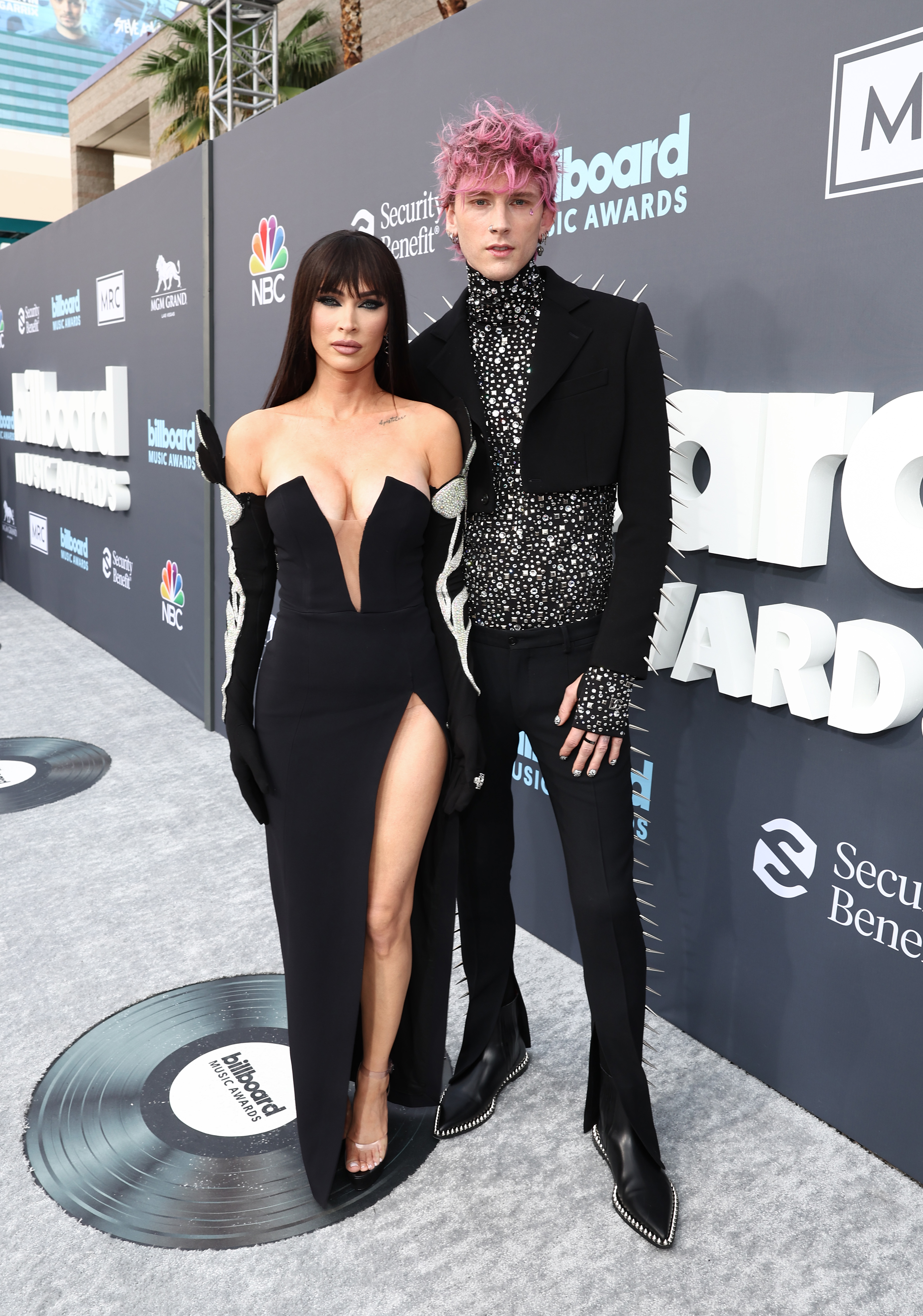 2022 Billboard Music Awards – Arrivals Megan Fox usando vestido preto com fenda lateral e luvas e Machine Gun Kelly todo de preto no Billboard Music Awards 2022