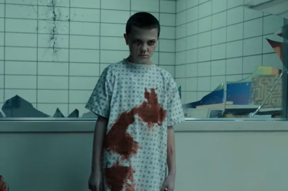 Eleven, de Stranger Things, com roupa manchada de sangue em laboratório