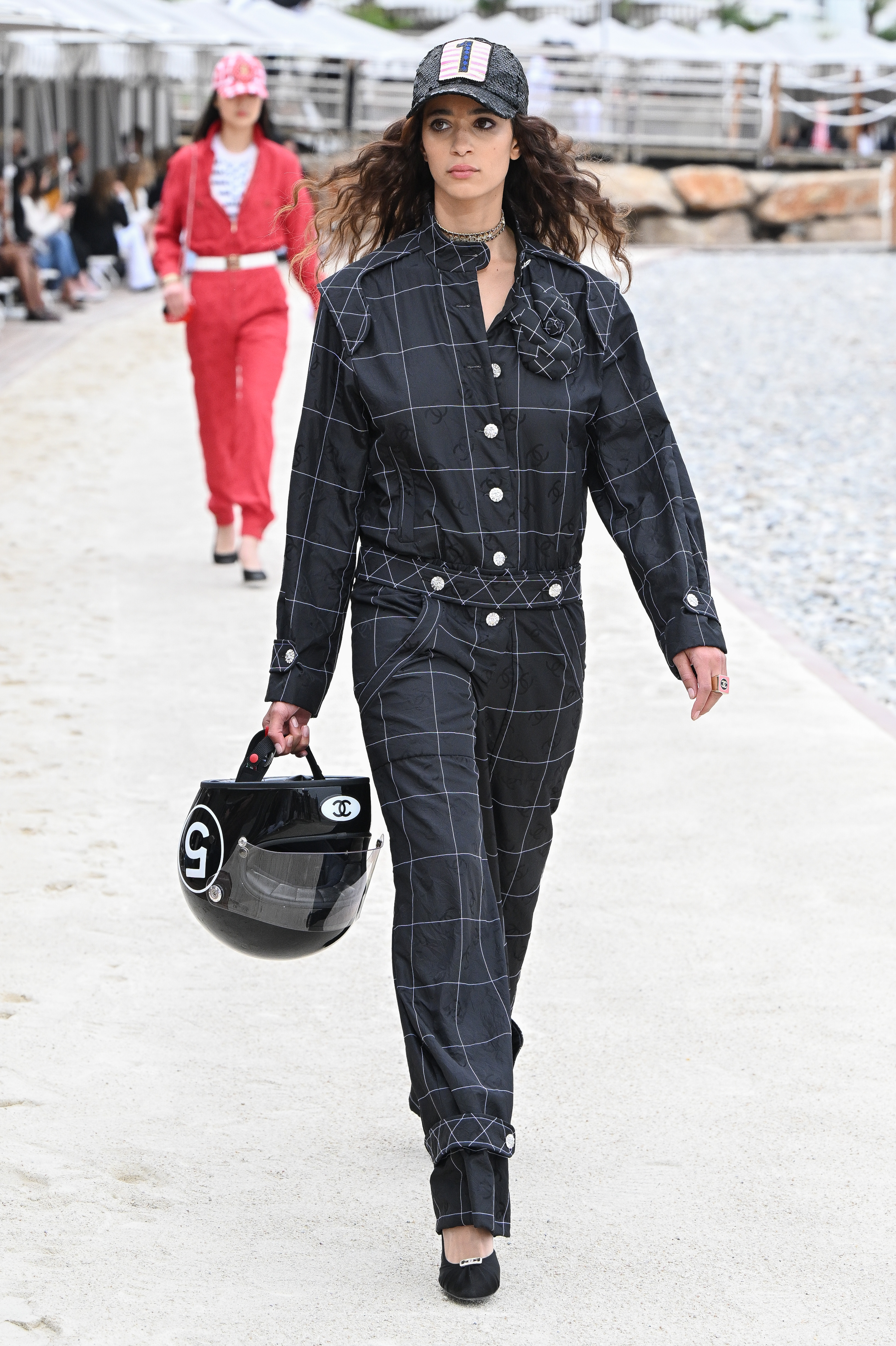 Chanel Cruise 2023 Collection : Runway In Monte-Carlo Modelo usando macacão preto, segurando capacete em desfile Chanel Cruise 2023 em Monte-Carlo, Mônaco