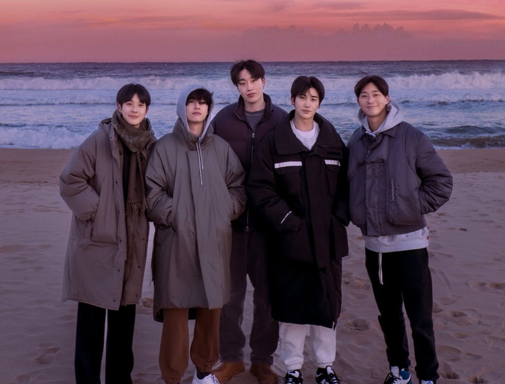 Imagem de divulgação de In The Soop Friendcation com os participantes da produção posando em uma praia com agasalhos e sorrindo levemente enquanto colocam as mãos no bolso