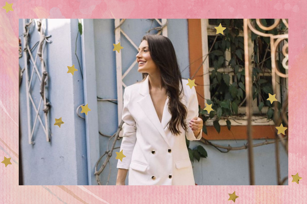 Montagem em fundo rosa com estrelinhas douradas de foto de garota usando blazer branco, olhando para o lado e sorrindo