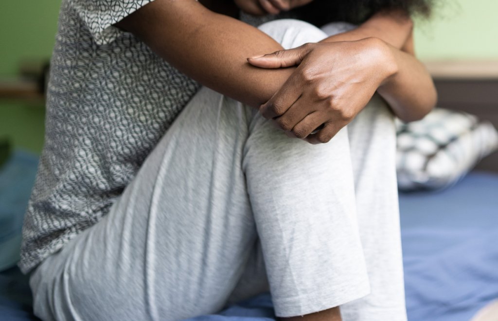 Mulher sentada, abraçando os joelhos, como se estivesse triste ou com dor