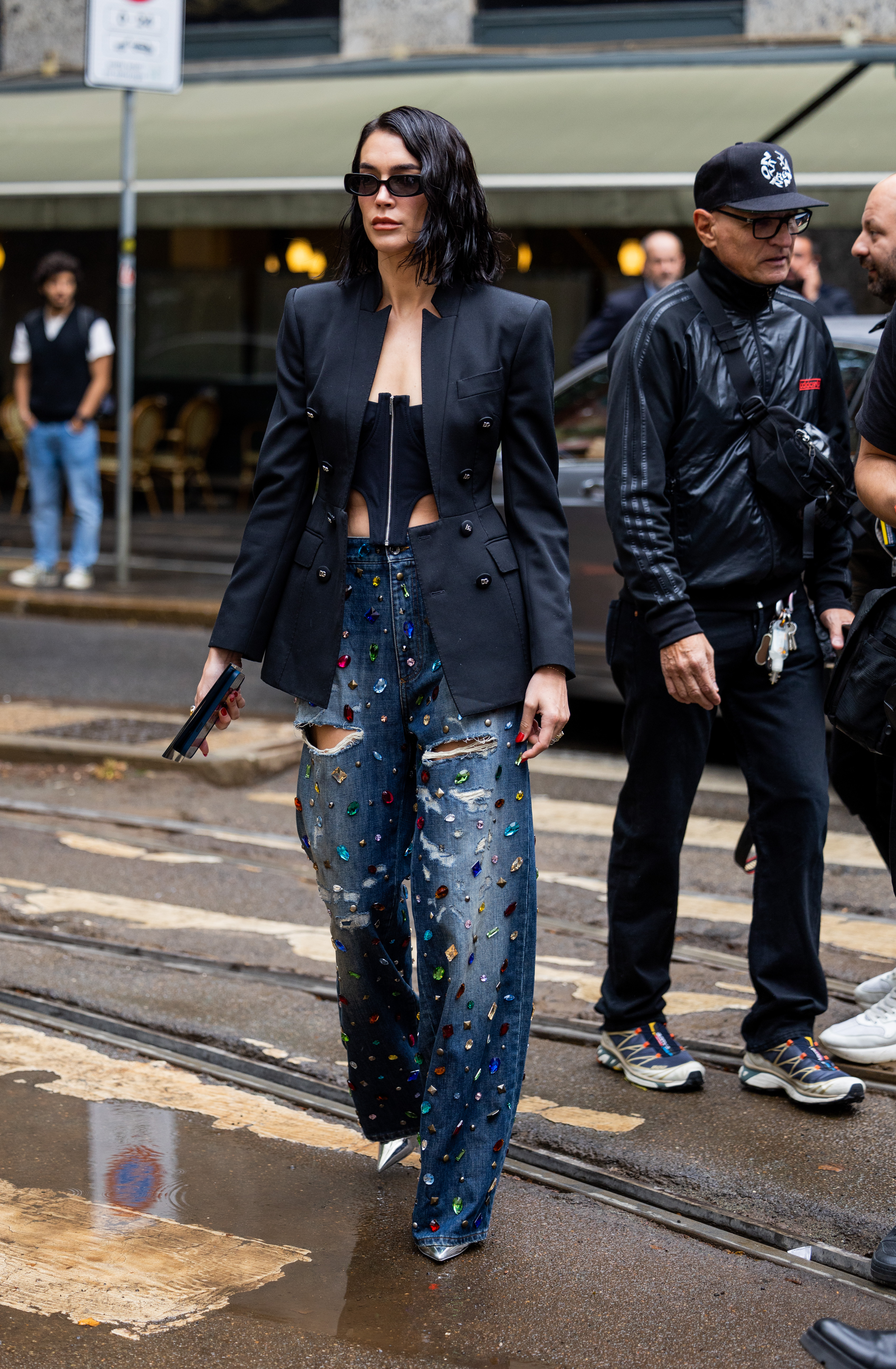 StreetStyle – Day 5 – Milan Fashion Week Womenswear Spring/Summer 2023 Mulher usando blazer e corset preto com calça jeans com aplicações de pedras coloridas no street style da semana de moda de Milão