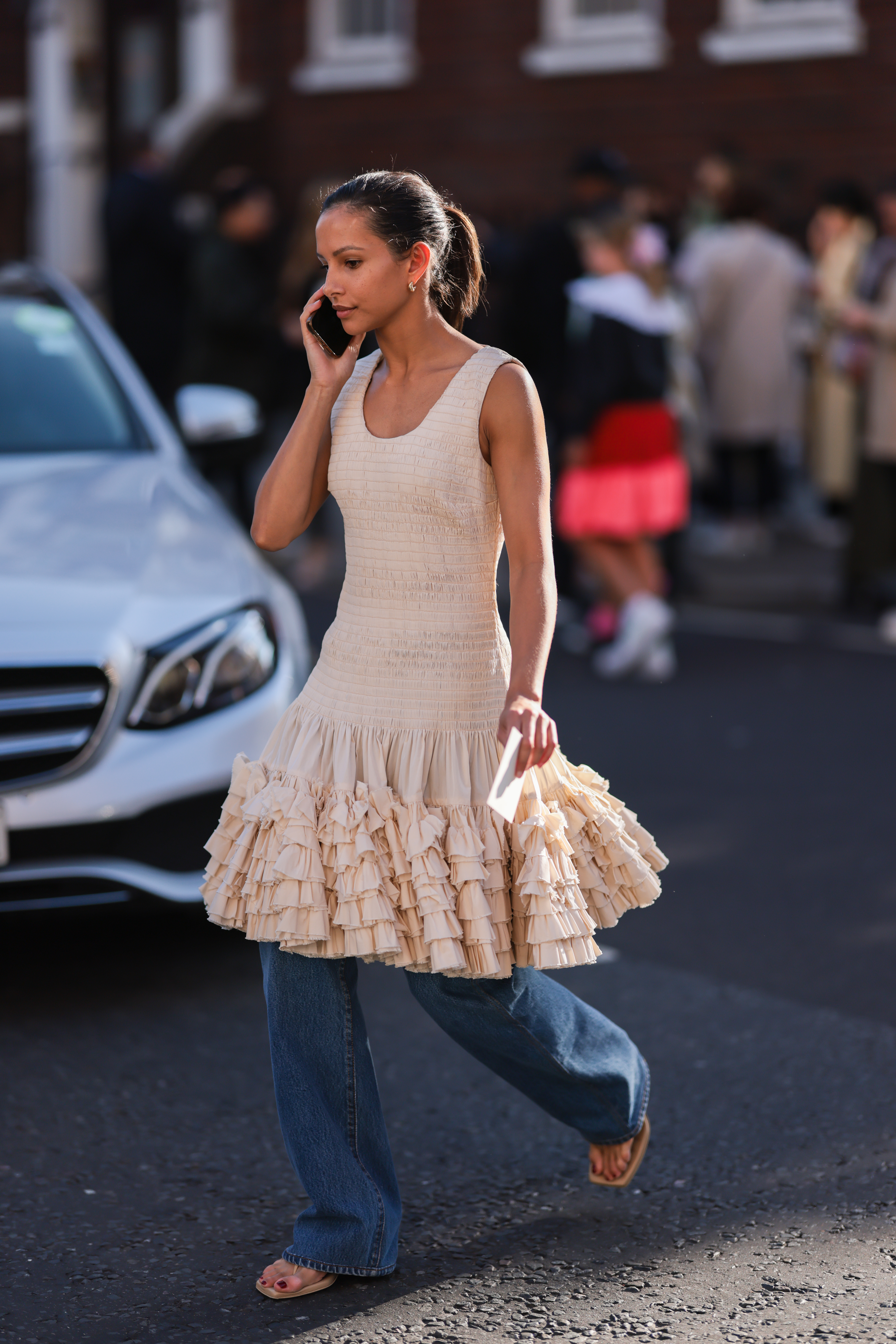 Street Style – LFW September 2022 Mulher usando vestido rosa claro de babados por cima de calça jeans enquanto anda na rua na semana de moda de Londres