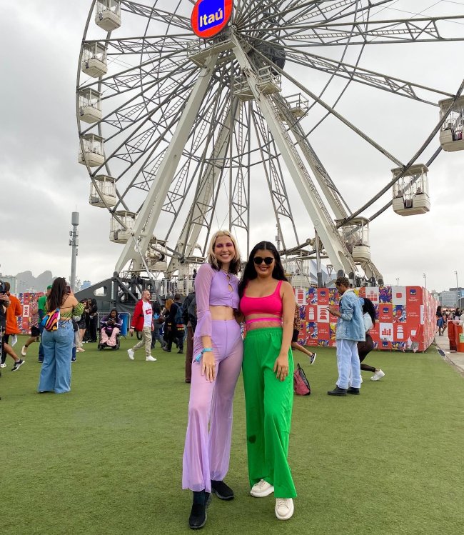looks-coloridos-rock-in-rio-2022 Foto de duas meninas no Rock in Rio 2022. Ela usam looks coloridos, olham para a câmera e sorriem.