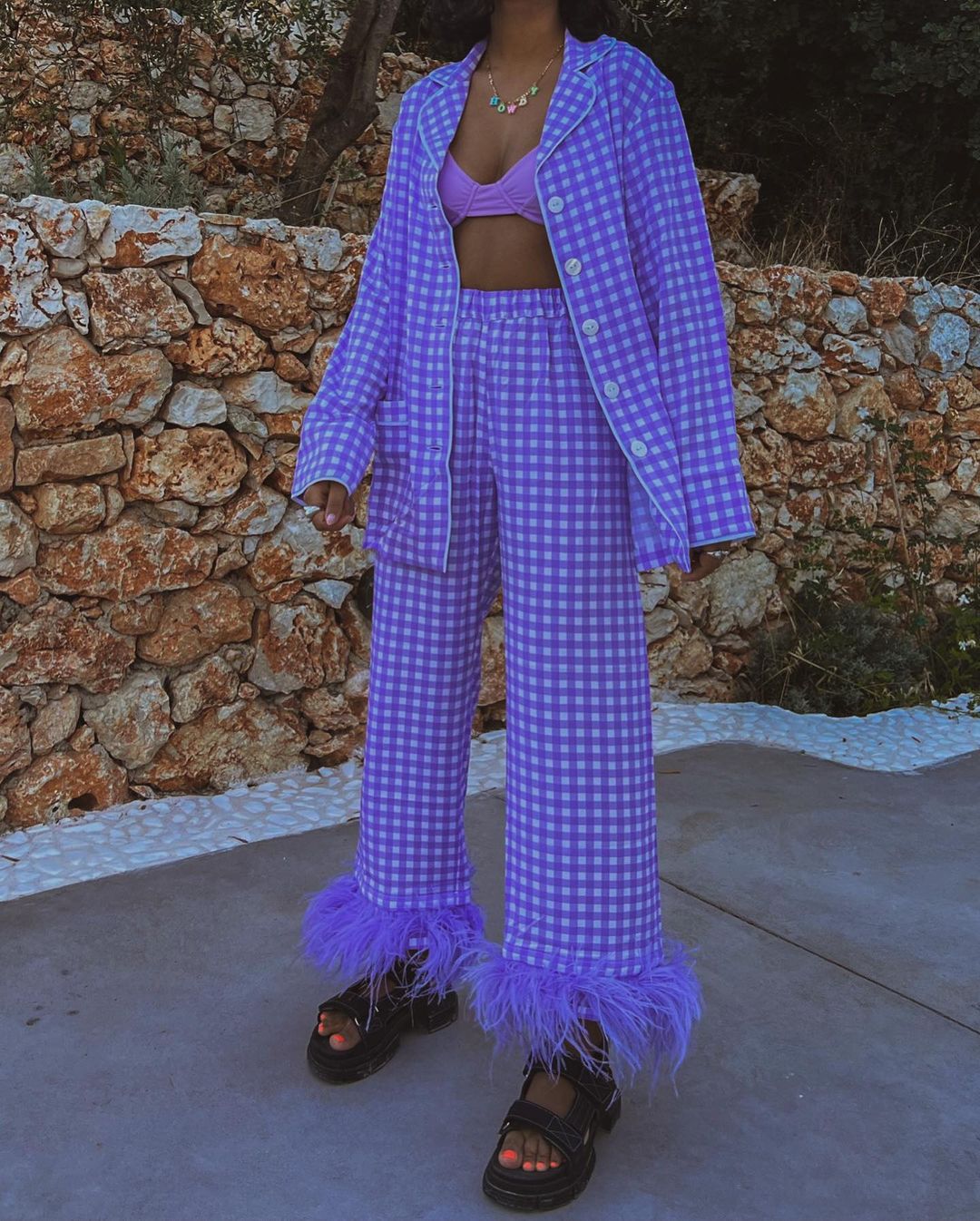 tendencia-primavera-2022-plumas Garota usando conjuntinho xadrez lilás com top da mesma cor e calça de plumas na barra, além de papete preta