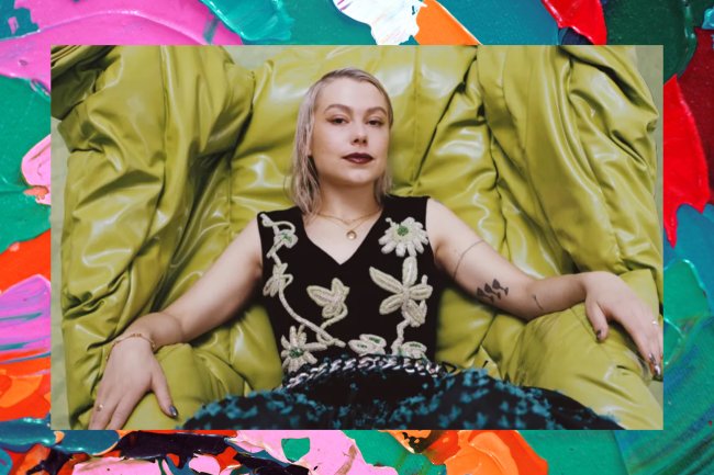 Phoebe Bridgers Fotografia de Phoebe Bridgers em um ensaio para a Teen Vogue. Ela está com o cabelo platinado, usando um vestido presto e está sentada em uma poltrona grande e verde de couro.