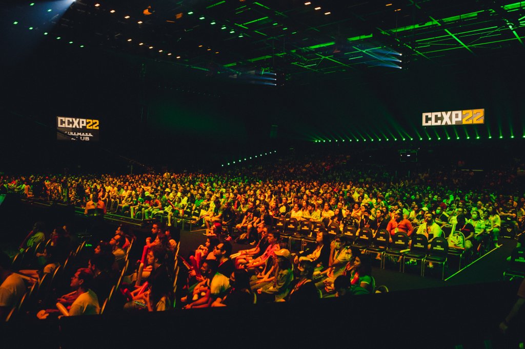 Público da CCXP em auditório iluminado por luzes verdes e amarelas