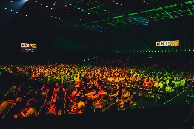 Público da CCXP em auditório iluminado por luzes verdes e amarelas