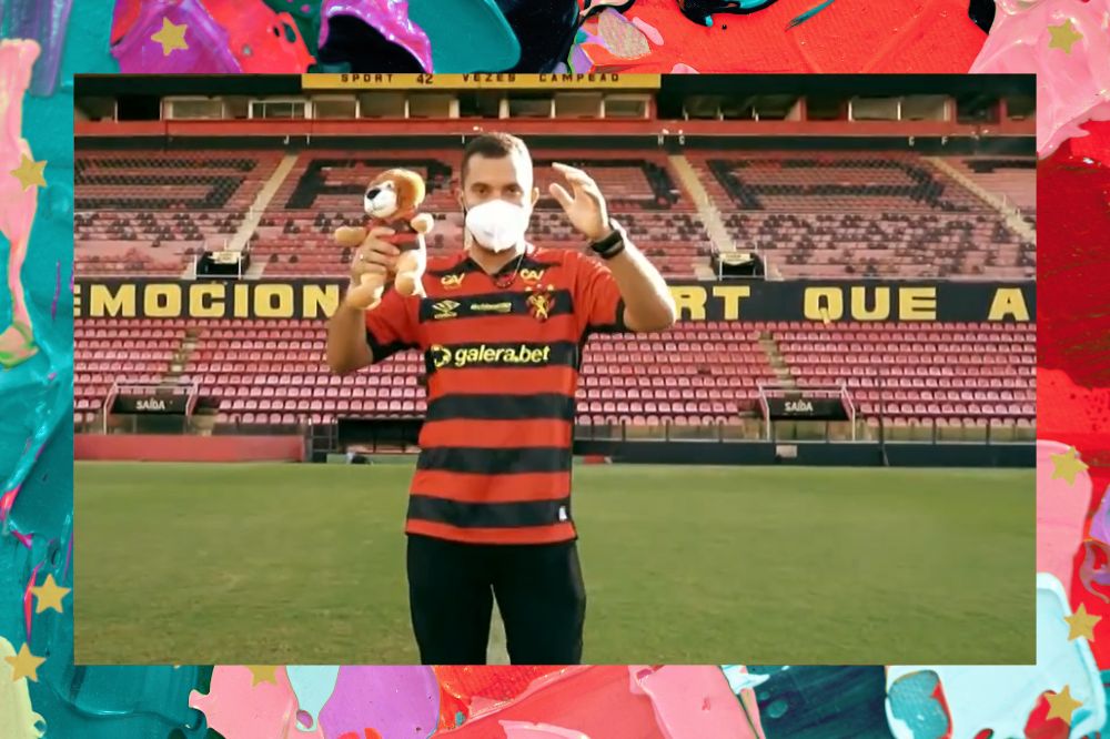 Gil do Vigor com a camisa do Sport Clube de Recife segurando um ursinho de pelúcia no estádio; a margem é uma textura nas cores vermelho, preto, azul, roxo e rosa; estrelas amarelas decoram a imagem