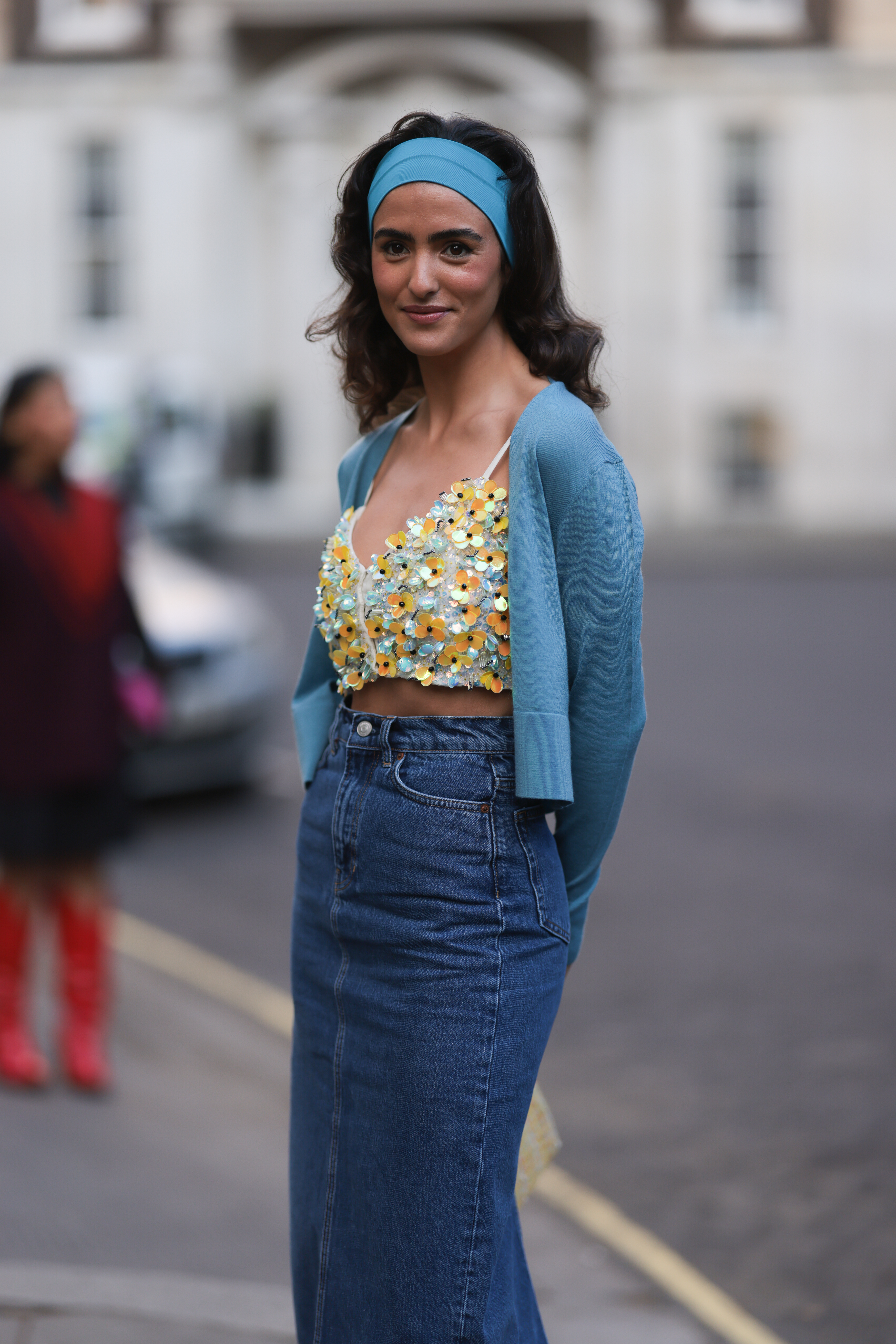 Street Style – LFW February 2023 Juny Breeze usando saia jeans, top floral, casaquinho azul e faixa de azul no cabelo no street style da semana de moda de Londres