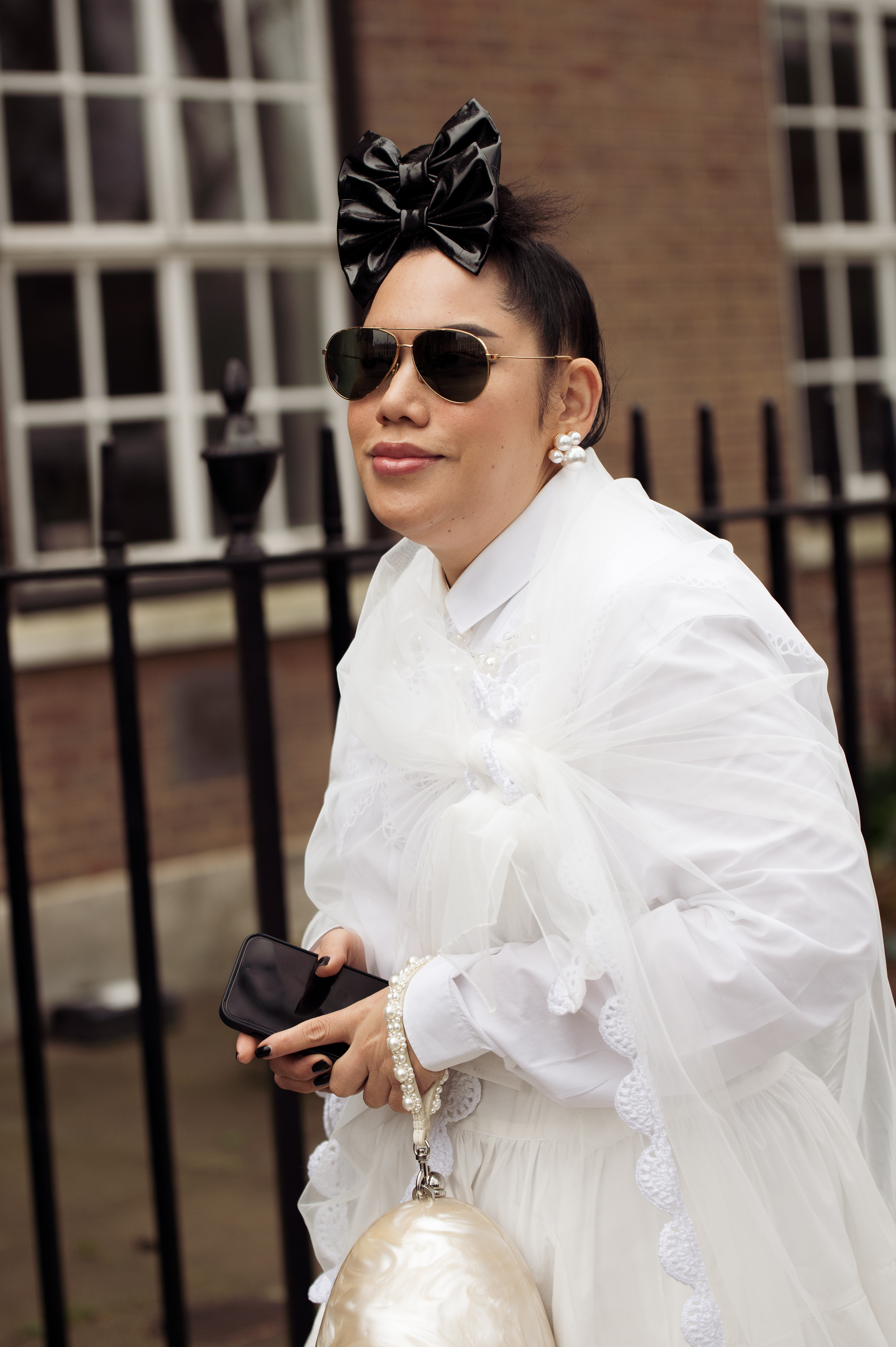 Street Style – LFW February 2023 Mulher usando look branco, óculos de sol e laços pretos na frente do cabelo no street style da semana de moda de Londres