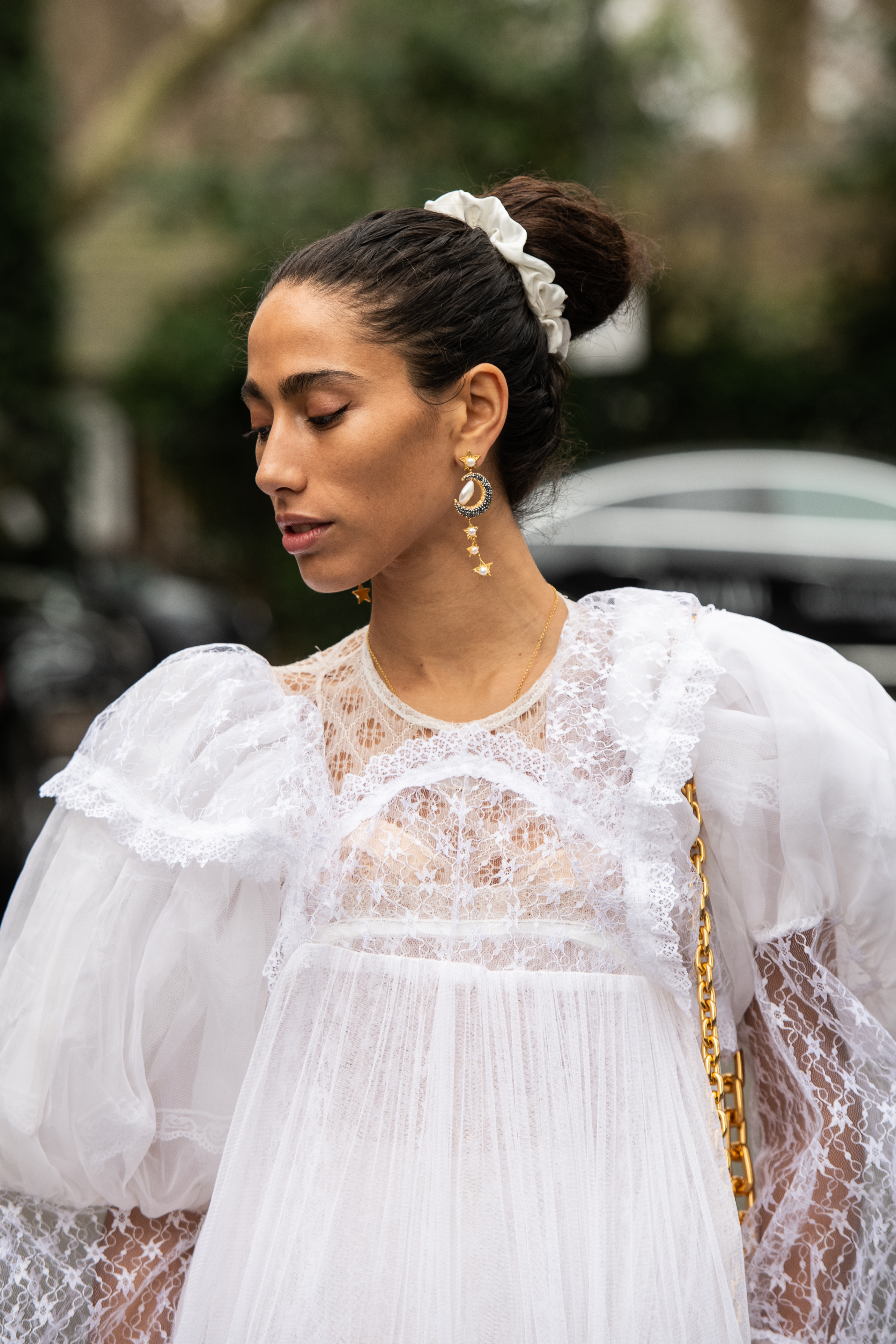 Street Style – LFW February 2023 Mulher usando vestido de renda branco e cabelo preso em coque envolto com srunchie no street style da semana de moda de Londres