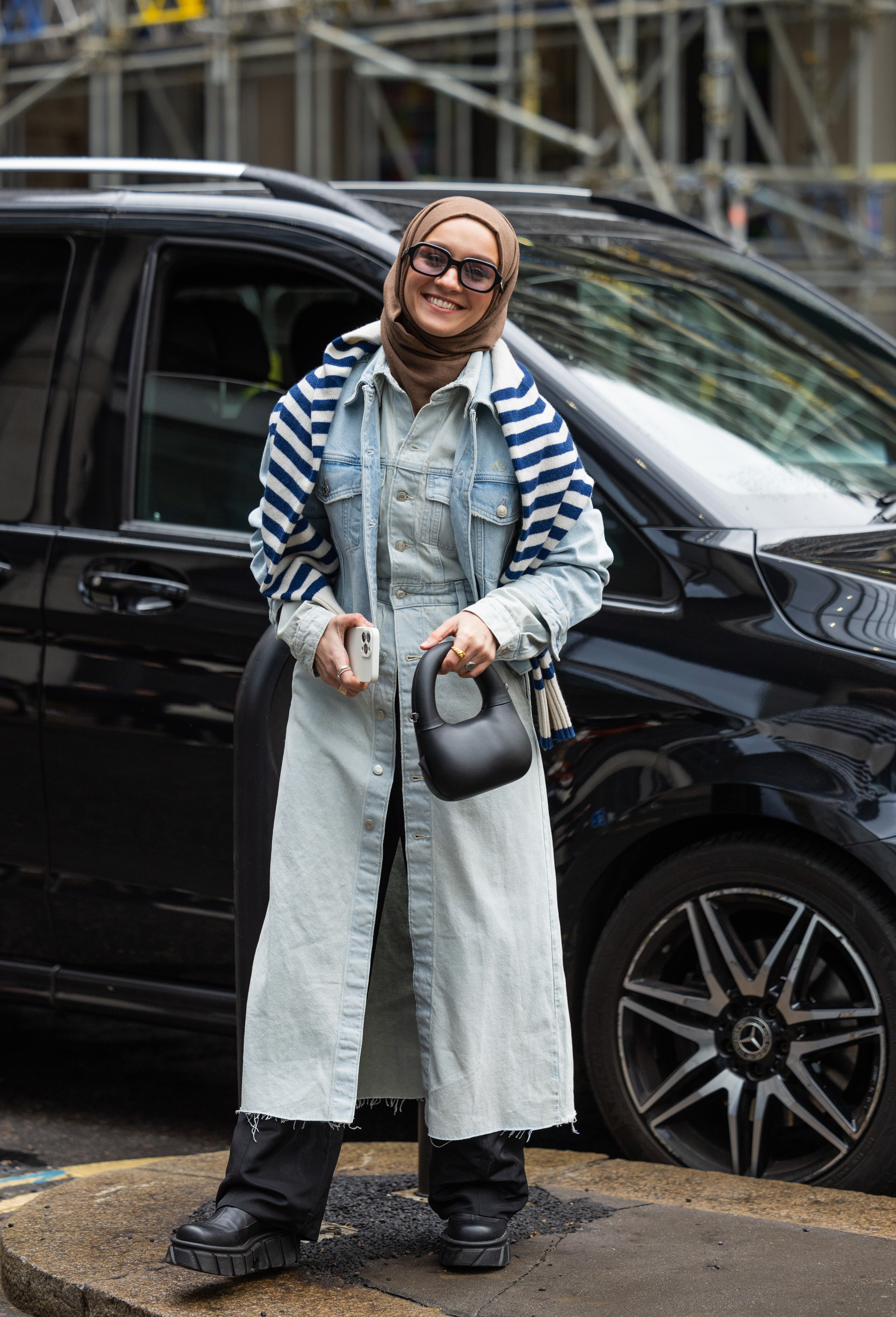 Street Style – LFW February 2023 Mulher usando usando vestido jeans por cima de calça preta no street style da semana de moda de Londres
