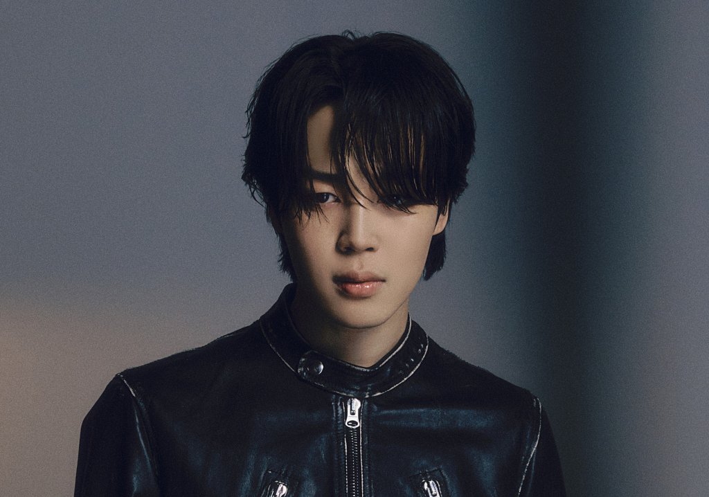 Jimin posando para foto em um fundo preto com expressão neutra