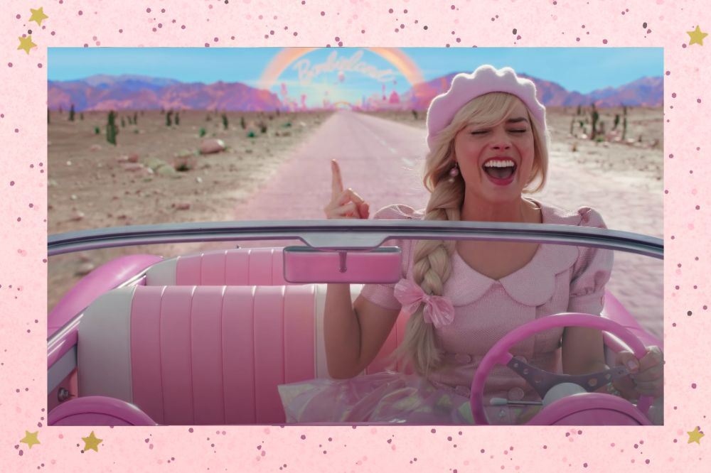 barbie Margot Robbie caracterizada como Barbie enquanto dirige um carro e canta com um dos dedos levantados; a Barbie lândia e um pôr-do-sol estão ao fundo; a margem é uma textura rosa com bolinhas e estrelas amarelas