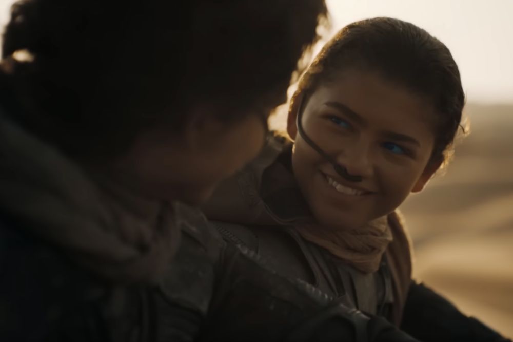 Zendaya caracterizada como Chani, sua personagem, e sorrindo em cena de Duna: Parte 2 enquanto olha para personagem Paul Atreides, interpretado por Timothée Chalamet